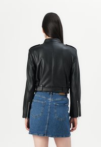 Svart lærjakke med cropped design, epauletter på skuldrene og beltehemper. Parret med et blått denimskjørt med baklommer.