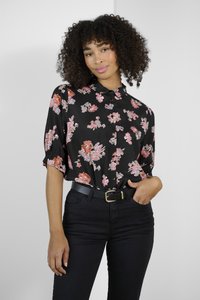 Blouse noire à motifs floraux roses et orange, avec fermeture à boutons et manches courtes bouffantes, accompagnée de jeans noirs taille haute et d'une ceinture.