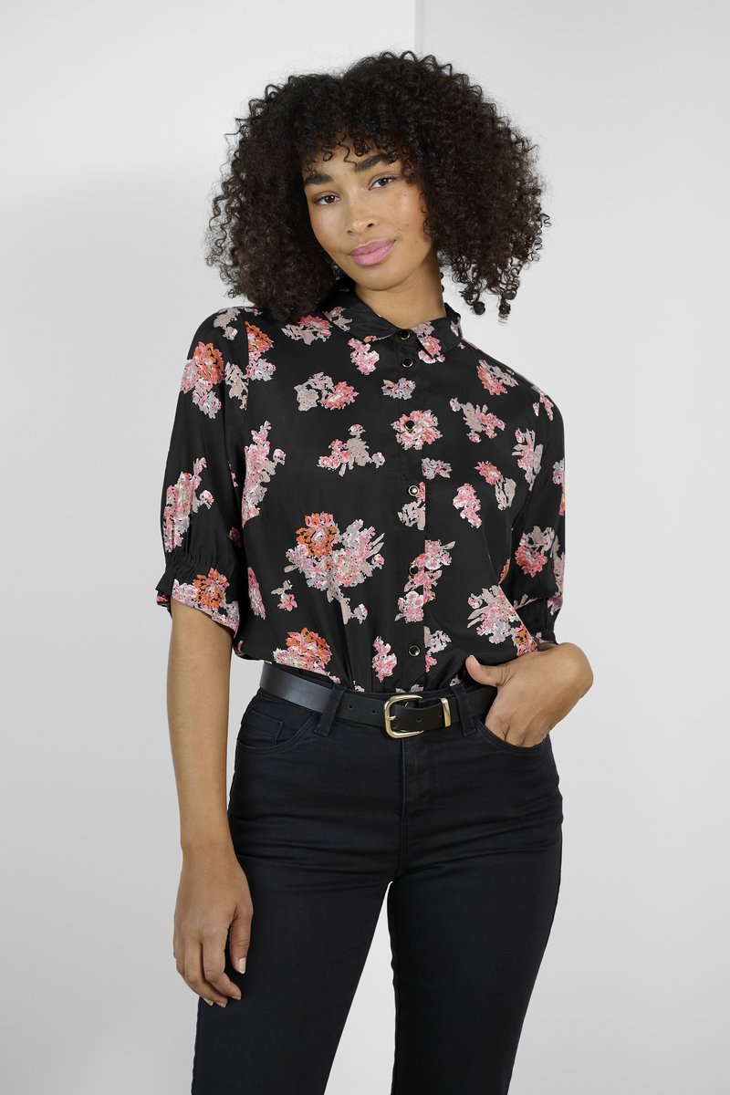 Blouse noire à motifs floraux roses et orange, avec fermeture à boutons et manches courtes bouffantes, accompagnée de jeans noirs taille haute et d'une ceinture.