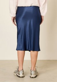 Jupe midi en satin bleu marine avec une texture lisse et un ourlet légèrement évasé, associée à des chaussures de sport grises. Pas de motifs ni de détails visibles.
