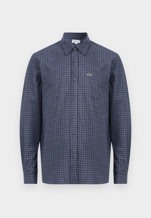 Camisa de manga larga a cuadros en azul marino con cuello puntiagudo y cierre de botones. Presenta un pequeño logotipo verde sobre el bolsillo izquierdo.