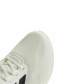 Zapato deportivo blanco y liviano con parte superior de malla texturizada, acento negro y suela acolchada. Cuenta con cordones y puntera reforzada.