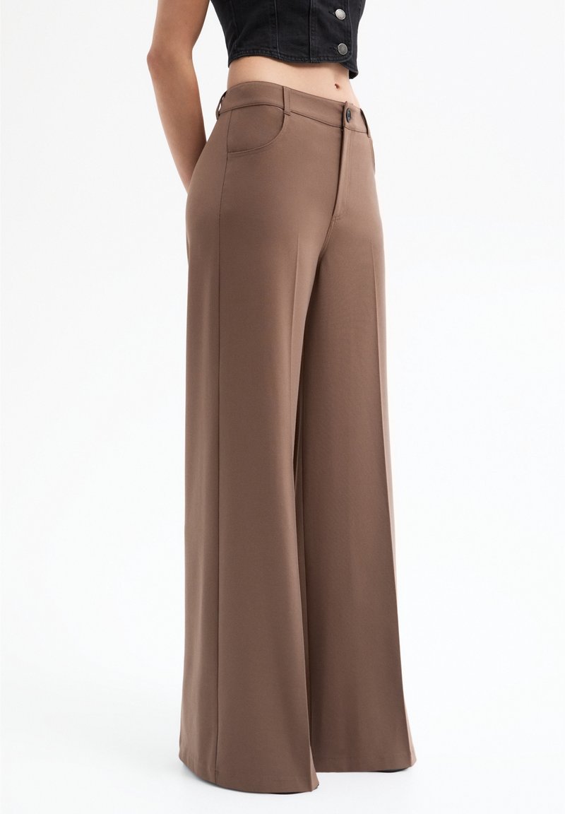Hnědé kalhoty s širokými nohavicemi z hladké látky, s knoflíkovým zapínáním a předními kapsami, které předvádějí upravený střih a splývavou siluetu.