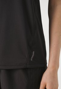 Černý sportovní top vyrobený z texturované tkaniny, s krátkými rukávy a malým logem "AEROREADY" poblíž lemu. Jednoduchý a funkční design.