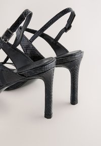 Sandale negre cu toc înalt, realizate dintr-un material texturat cu model de piele de șarpe, având bretele subțiri și închidere cu cataramă.