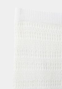 Gros plan d'un tissu tricoté texturé blanc avec bord côtelé, montrant un motif de tissage ouvert détaillé et un matériau doux.