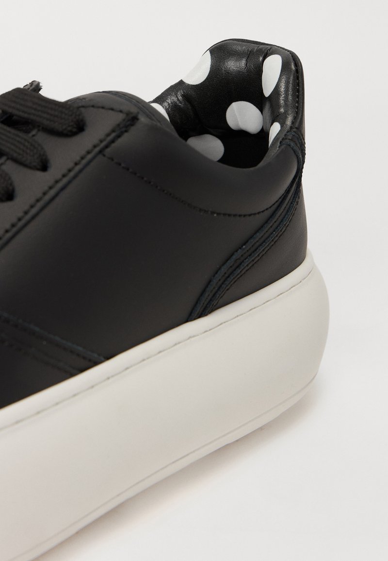 Zwarte leren sneaker met een witte rubberen zool. Interieur heeft een zwarte voering met witte stippen. Vetersluiting ontwerp met grove textuur.