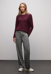 Bordeauxfarvet striktrøje med lange ærmer kombineret med grå bukser med tynde striber og hvide sneakers. Trøjen har en rund halsudskæring.