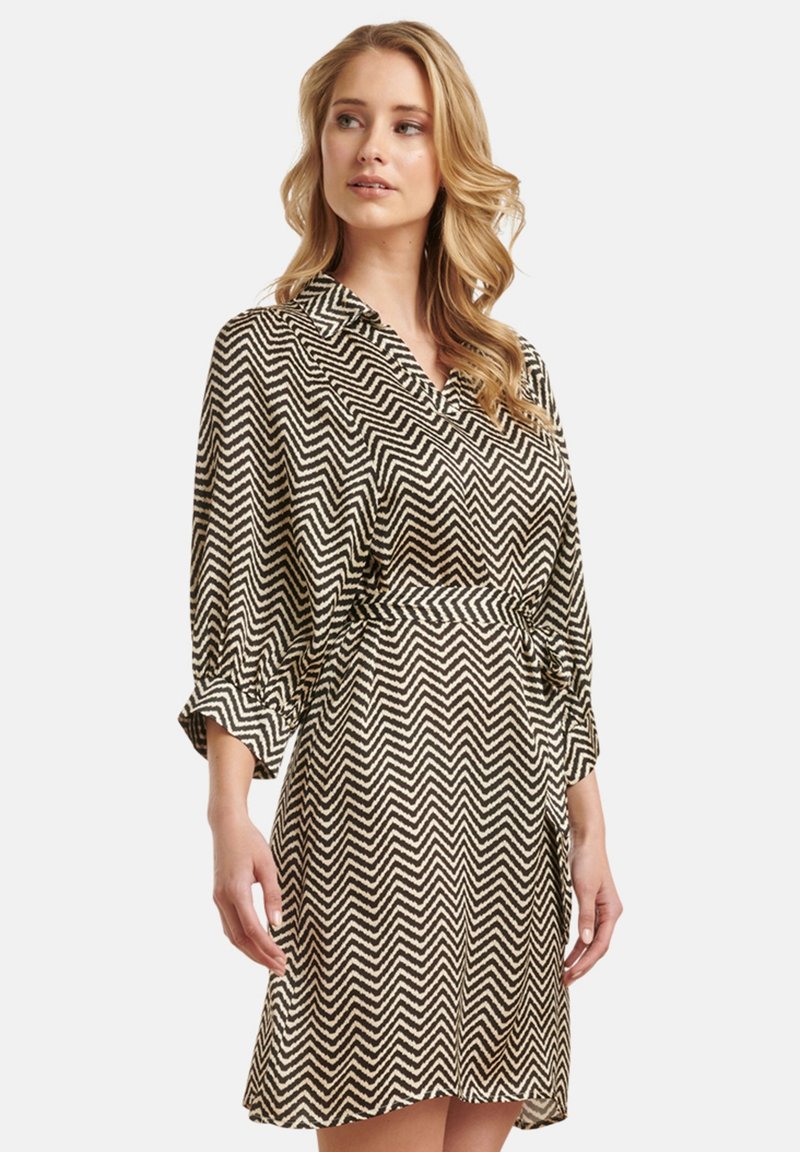 Schwarz-weißer, im Zickzack-Muster gestalteter Kleid mit kragenförmigem Ausschnitt, 3/4-Ärmeln und geraffter Taille. Leichter Stoff mit glatter Textur.