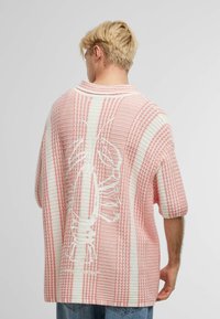 Overdimensjonert strikkegenser i rosa og hvitt med stripete mønster; har et hummerdesign på baksiden og korte rullede ermer.