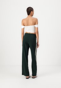 Witte off-the-shoulder crop top gecombineerd met donkergroene broek met brede pijpen en een zijstreepdetail. Glad materiaal, casual pasvorm.