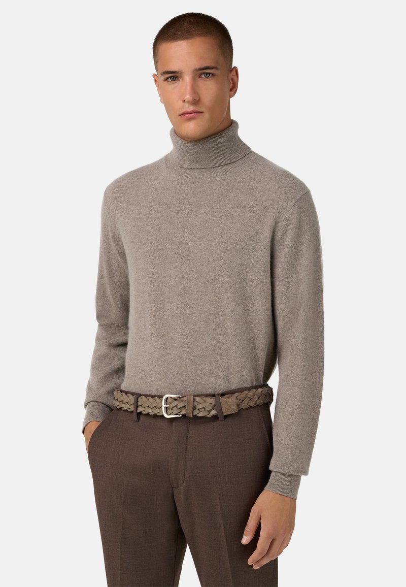 Pull col roulé marron clair en tissu doux, associé à une ceinture tressée dans un ton vert-brun atténué. Un pantalon marron vient parfaire la tenue.