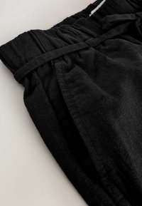 Fekete anyagú, laza szabású nadrág, elasztikus derékpánttal és megkötő részlettel, sima textúrával és minimális varrással.