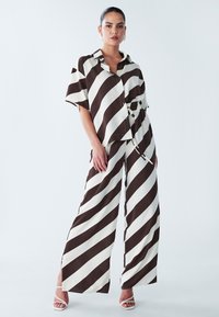 Gestreiftes Zweiteiliges Outfit mit einem locker sitzenden braunen und weißen Hemd mit Kragen und passenden weit geschnittenen Hosen mit seitlichen Schlitzen.