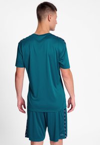 Teal idrottströja med korta ärmar och rund halsringning, kombinerad med matchande shorts som har sidopaneler och mönstrade detaljer.