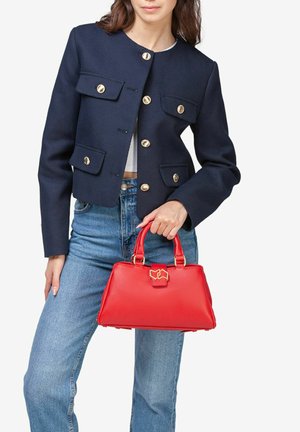 Rode leren handtas met een gestructureerde vorm, gouden hardware accenten, een bovenste handvat en een sluitingdetail. Draagt bij een marineblauwe jas en jeans.