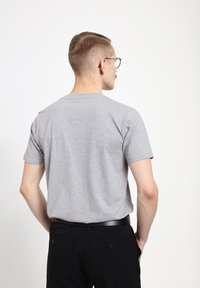 Šedé bavlněné tričko s krátkým rukávem, kulatým výstřihem a jednoduchým designem. Nosené s černými kalhotami s dvěma zadními kapsami.