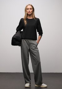 Czarna bluzka z długim rękawem i bufkami na ramionach, szare szerokie spodnie w prążki, białe trampki oraz czarna pikowana kurtka zarzucona na ramię.