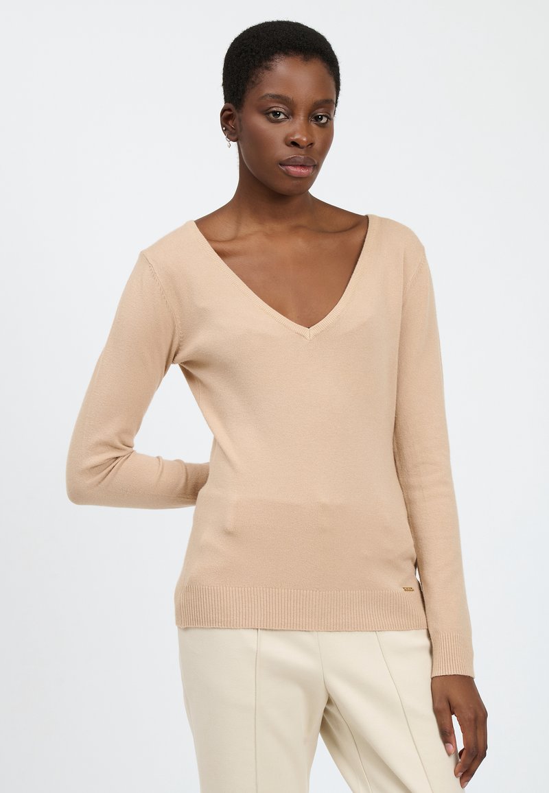 Beige V-Ausschnitt-Pullover mit langen Ärmeln, aus weichem, strukturiertem Stoff. Gerippter Saum und Bündchen, mit einem subtilen Logodetail an der Seite.