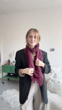 Bordó sál puha anyagból, a nyak köré tekerve, fekete blézerrel és bézs nadrággal párosítva, egy világos, minimális berendezésű szobában.