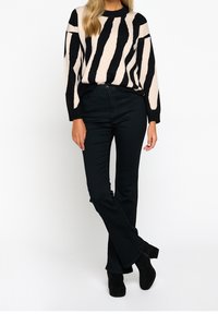 Suéter de rayas negras con un ajuste relajado, combinado con jeans oscuros. Tejido texturizado, puños anchos y jeans de cintura alta con un ligero acampanado.