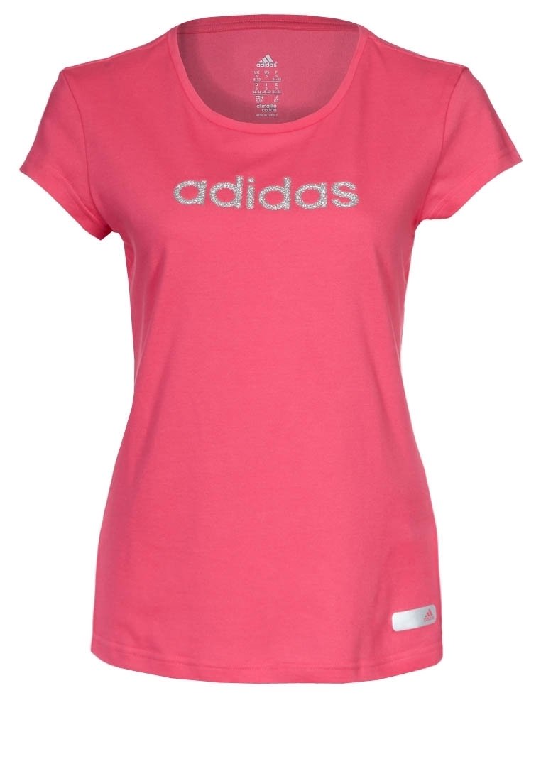 Camiseta de manga corta rosa, hecha de algodón, con cuello redondo. Presenta el logo plateado de "adidas" en el pecho y una pequeña etiqueta en la parte inferior.