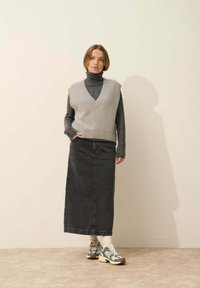 Szary wełniany kamizelka na ciemnoszarym golfie, w połączeniu z długą czarną spódnicą dżinsową i wzorzystymi trampkami. Gładka faktura, dekolt w kształcie V.