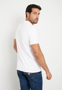 T-shirt blanc à manches courtes, en tissu doux, col rond, style ajusté. Jean en denim bleu avec un patch logo sur la poche arrière.