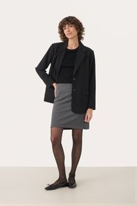 Schwarze Blazer über einem schwarzen Oberteil, kombiniert mit einem grau karierten Rock. Schwarze transparente Strumpfhosen und schwarze Ballerinas runden das Outfit ab.