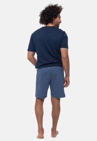 Navyblauwe T-shirt en blauwe geruite shorts. T-shirt heeft een klassieke snit, shorts zijn knielang met een gestructureerd patroon. Voeten bloot.