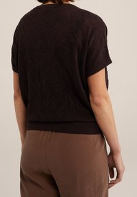 Černý krátký svetr s texturovaným vzorem vln na pletenině a žebrovaným lemem, doplněný volnými hnědými kalhotami.