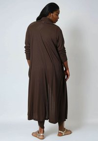 Long brown cardigan with a ribbed texture, featuring a high neck and long sleeves, extending to mid-calf with side slits. Minimalistic design.