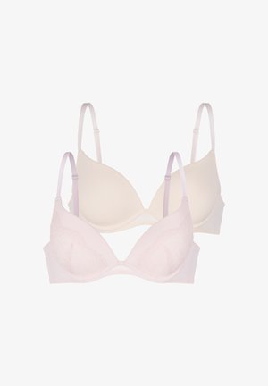 Vrouw met lang, donker haar die een lichtroze kanten push-up beha draagt tegen een effen grijze achtergrond.