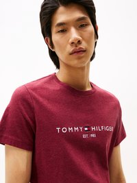 Bordová tričko vyrobené z bavlnenej zmesi, s okrúhlym výstrihom a krátkymi rukávmi. Na prednej strane je umiestnené logo "TOMMY HILFIGER EST. 1985" v bielej a červenej farbe.