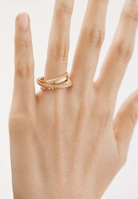 Tres anillos de oro entrelazados en una mano; uno cuenta con pequeñas piedras, otro tiene un acabado liso y el tercero presenta un diseño texturizado.