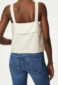Weißes Leinen-Top mit stufenförmigem Design und breiten Trägern, kombiniert mit blauen Jeans aus Denim mit Gesäßtaschen und einer figurbetonten Silhouette.