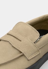 Beige velúr loafer cipők, lapos, kerek orral és dekoratív, kivágott felső pánttal, fekete talpon. Puha tapintású.