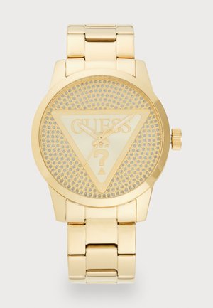 Orologio da polso in tono oro con quadrante triangolare, texture a rilievo e logo "GUESS" inciso. Presenta un bracciale metallico abbinato e una corona.