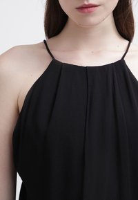 Haut noir à col licou avec fines bretelles, présentant des plis le long du décolleté, une texture douce et une silhouette fluide.