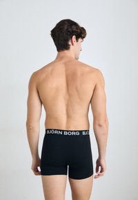 Schwarze Boxershorts aus Baumwolle mit einem elastischen, markierten Bund. Die Ansicht zeigt die Rückseite einer männlichen Figur ohne T-Shirt.