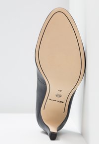 Chaussure à talon haut en cuir noir à bout pointu, vue de la semelle avec la taille 37 et le nom de la marque "Tamaris".