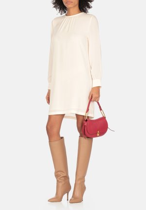 Abito crema a maniche lunghe con scollatura plissettata, abbinato a stivali beige alti fino al ginocchio e una borsa rossa strutturata con hardware dorato.