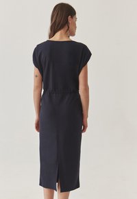 Navyblauwe midi-jurk met kapmouwen, taillering en een split aan de achterkant. Zachte, gladde stof met subtiele textuur en een ontspannen design.