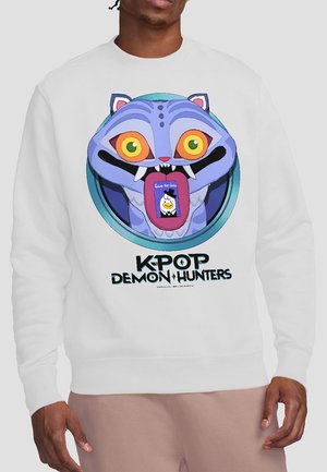 Person wearing white sweatshirt with a colorful cartoon cat face, large eyes, and fangs holding a "Save the date" card on its tongue.