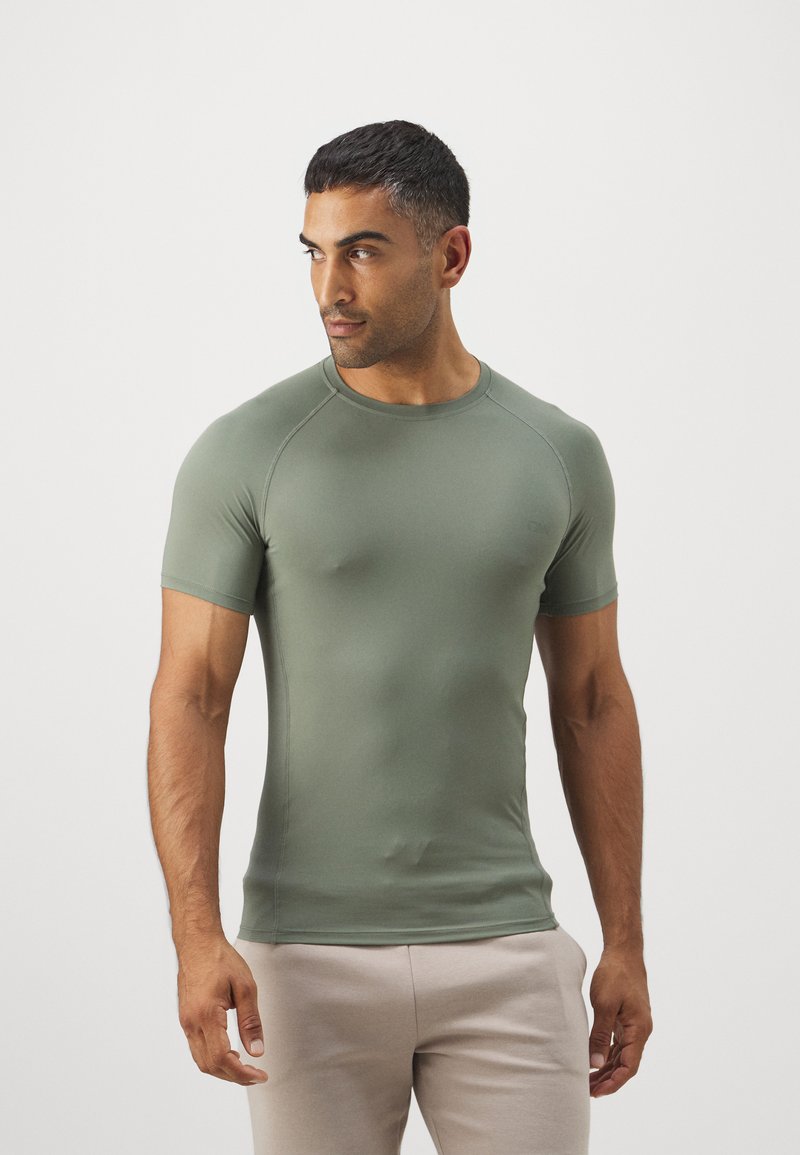 Īsām piedurknēm olīvzaļš krekls, kas izgatavots no elastīga auduma, ar pieguļošu dizainu, apaļu kakla izgriezumu un raglana piedurknēm papildu komfortam.