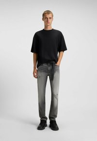 Black ribbed t-shirt with short sleeves, paired with light gray distressed jeans featuring rips. Model wears black shoes. Simple design.