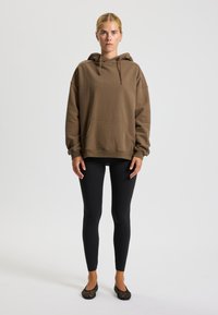 Felpa marrone con cappuccio, tasca frontale, vestibilità comoda e maniche lunghe. Abbinata a leggings neri e ballerine nere in rete.