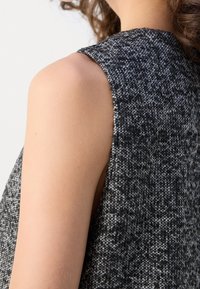 Gros plan sur l'épaule et le haut du bras d'une personne portant un haut sans manches en tissu texturé noir et blanc.