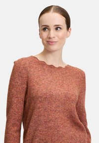 Texturierter Wollpullover in warmen Rosa- und Orangetönen, mit gekerbt geschnittenem Ausschnitt und langen Ärmeln, der eine leicht taillierte Silhouette aufweist.