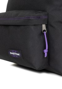 Zwarte stoffen rugzak met een voorvak met een paarse ritstrekker en stiksel. Eastpak-logo patch zichtbaar aan de onderkant aan de voorkant.